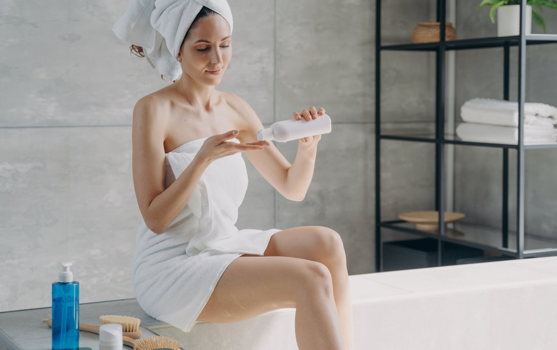 A woman is putting some body lotion as she sits on her bathtub.