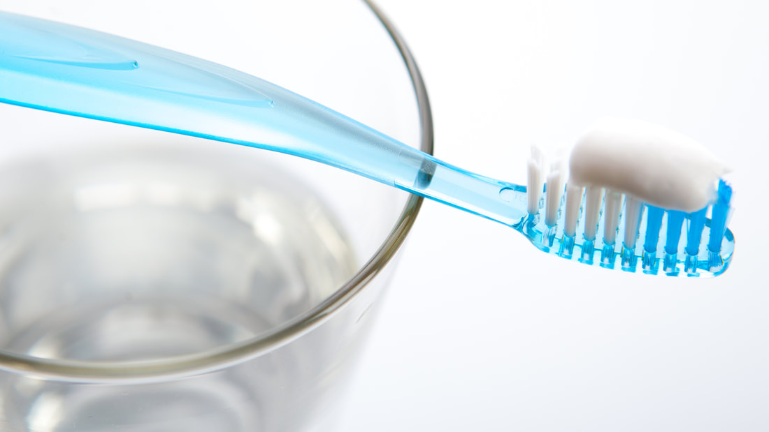 A toothbrush with toothpaste on it is being showcased here as it sits on a glass of water.
